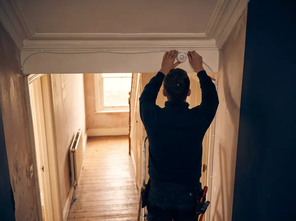 An alarm engineer on a stepladder connecting a cable to a ceiling-mounted motion sensor